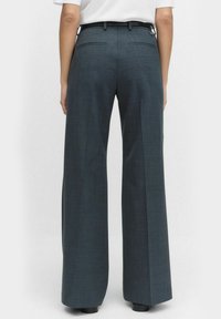 Weite Hose aus dunkelgrauem Stoff, mit flachem Vorderteil, Gürtelschlaufen und zwei Gesäßtaschen. Der Stoff hat eine dezente Textur.