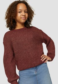 Gestrickter kastanienfarbener Pullover mit strukturiertem Muster, rundem Halsausschnitt und lässiger Passform. Kombiniert mit einem blauen Jeansrock.