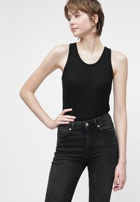 Manga larga preta com nervuras combinada com jeans pretos de cintura alta com um padrão texturizado e embellishments nos bolsos da frente.