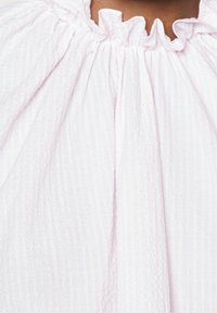Top de color rosa claro con una tela texturizada y arrugada. Cuenta con un escote con volantes y un diseño fluido, creando caídas suaves.