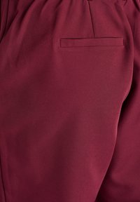 Maroon trouser fabric with a smooth texture, featuring a discreet back pocket and gathered waistband.