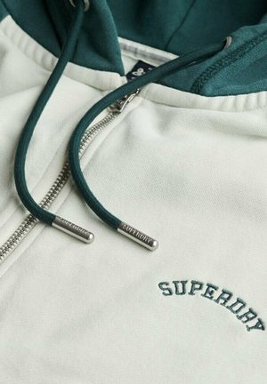 Witte hoodie met ritssluiting en groene capuchon en koordjes. "SUPERDRY" in het groen gedrukt op de borst. Metallic rits en accenten op de koordjes.