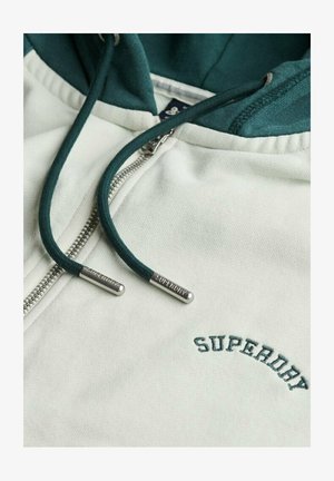 Biała bluza rozpinana z zielonym kapturem i sznurkiem. Na piersi zielonym kolorem nadrukowane słowo "SUPERDRY". Metalowy zamek błyskawiczny i akcenty sznurka.