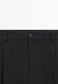 Pantalon noir habillé avec fermeture par bouton, passants pour ceinture et devant lisse, montré de la taille vers le bas sur fond blanc.