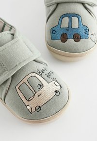 Hellgrüne Leinenschuhe mit Klettverschlüssen, die gestickte Auto-Motive aufweisen: ein blaues Auto und ein beiges Auto mit cartoonhaften Details.