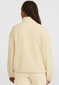 Pullover in pile color beige chiaro, con colletto alto e vestibilità morbida. Il tessuto testurizzato presenta un aspetto soffice con dettagli di cucitura sottili.