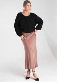 Schwarzer, strukturierter Strickpullover mit weiten Ärmeln, kombiniert mit einem glänzenden, blushfarbenen Satinrock. Das Model trägt schwarze, spitze Absatzschuhe und eine zarte Halskette.