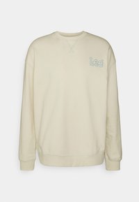 Krémový svetr s kulatým výstřihem, dlouhými rukávy a malým modrým vyšitým logem "Lee" na levé straně hrudi. Měkká textura.