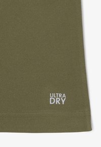 Olijfgroen, gestructureerde stof met "ULTRA DRY" in het wit op de zoom. Glad afgewerkt met een lichtgewicht, ademend ontwerp.