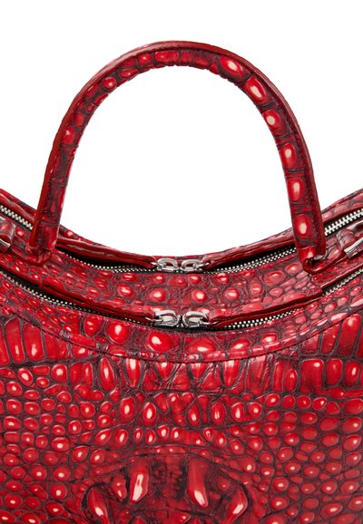 Anse et partie supérieure d'un sac à main rouge à texture crocodile brillante avec deux fermetures éclair argentées sur fond blanc.