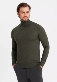 Pull à col roulé vert olive en tissu tricoté, avec des manches ajustées et un col côtelé au toucher lisse.