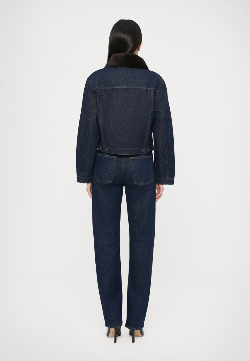 Jeansjacke mit dunkler Waschung, braunem Pelzkragen, lockerem Schnitt und Knopfverschluss an der Taille. Kombiniert mit passenden dunklen Jeans.