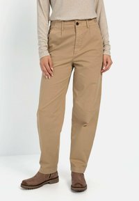Beige Baumwollhosen mit lockerer Passform, geraden Beinen, Fronttaschen und dezenten Nähdetails, kombiniert mit braunen Stiefeletten.