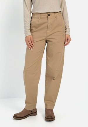 Beige katoenen broeken met een ontspannen pasvorm, rechte pijpen, voorzakken en subtiele stikdetails, gecombineerd met bruine enkellaarsjes.