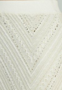 Jupe en tricot off-white avec un motif en chevron. Présente des détails texturés et des embellissements métalliques pour une dimension supplémentaire.