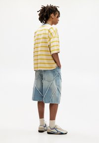 Striped short-sleeve yellow and white shirt, light blue distressed denim shorts with zigzag pattern, cream socks, and beige sneakers with blue accents.