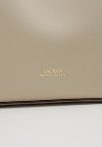 Beige kožená kabelka s hladkým povrchem, s embosovaným zlatým logem "LAUREN RALPH LAUREN" ve středu. Klasický obdélníkový tvar.