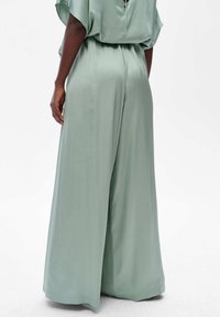 Wide-leg jumpsuit van zacht, mintgroen materiaal. Heeft een vloeiende silhoutte, korte mouwen en een sleutelgatdetail aan de achterkant. Soepele textuur.
