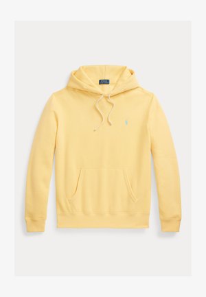 Dzeltena kokvilnas kapucīne ar izvelkamu kapuci, kangaroo kabatu, ribinātām piedurknēm un apakšmalu, kā arī mazu zilu logotipu uz krūtīm.