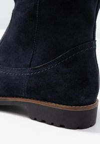 Navy samle boty ke kotníkům s texturovaným povrchem, featuring prošívaný šev a hnědou gumovou podrážku s drážkovaným vzorem pro lepší přilnavost.