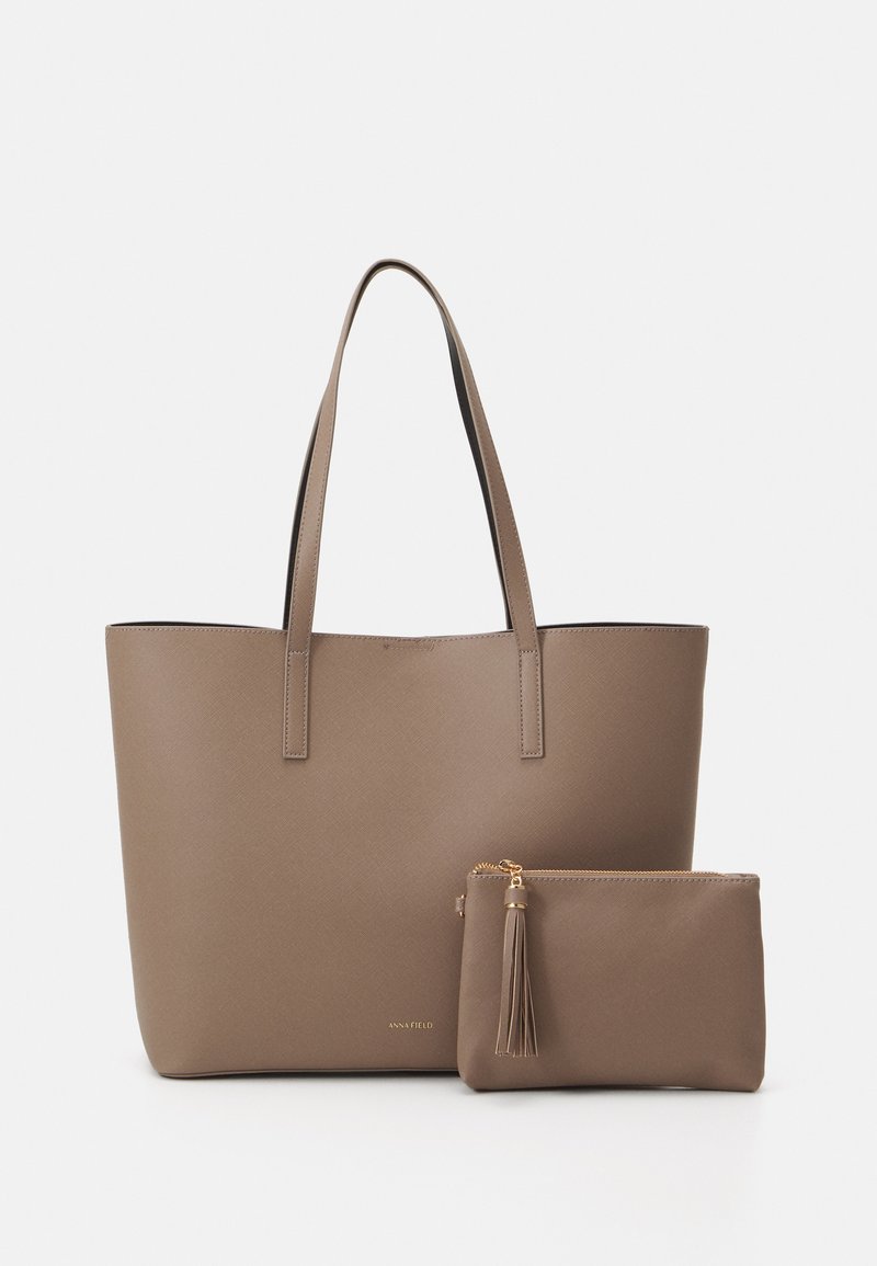 Bolso tote en material sintético color taupe mate con dos asas largas y un estuche con cremallera a juego, que presenta un acento de borlas para mayor detalle.