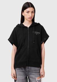 Melna rāvējslēdzēja sporta jaka no mīksta auduma ar kapuci, īsām piedurknēm ar aizdares pogām un priekšējām kabatām. Uz krūtīm ir logo.