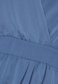 Tissu bleu avec un détail de couture froncée et une large ceinture, montrant des plis doux et une texture lisse.