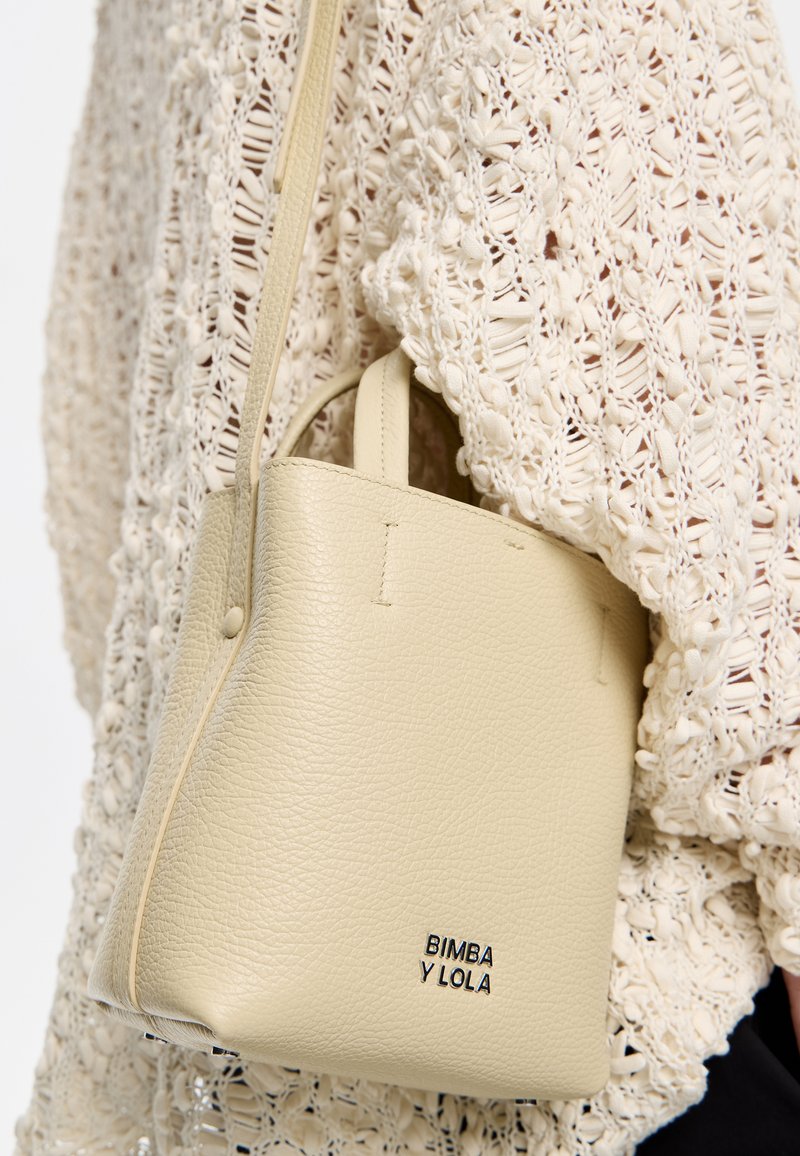 Bolso de cuero texturizado de color beige claro con asas cortas, forma rectangular y logotipo en relieve "BIMBA Y LOLA" en la parte frontal.