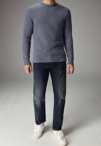 Maglione blu lavorato a maglia con scollo rotondo, polsini e orlo a coste. Abbinato a jeans in denim scuro e sneakers bianche.