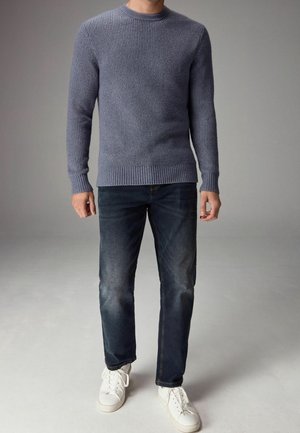 Gebreid blauw sweater met een ronde halslijn, geribbelde manchetten en zoom. Gepaard met donkere denim jeans en witte sneakers.