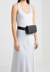 Borsa nera a cintura con una chiusura, caratterizzata da strisce metalliche diagonali. Realizzata in materiale liscio, fissata su una banda nera regolabile.