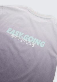 T-shirt avec un dégradé du violet clair au blanc et le texte « EASY-GOING ATTITUDE » imprimé en grandes lettres dans le dos.