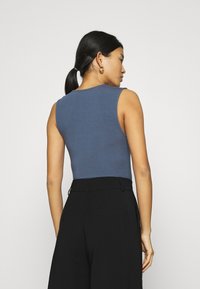 Top senza maniche, aderente, in tessuto blu scuro, con scollatura rotonda e texture liscia. Abbinato a pantaloni neri con vita alta.