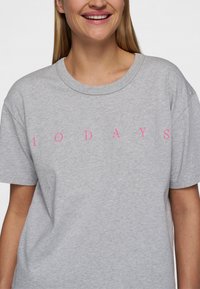 Camiseta de algodón gris con mangas cortas y cuello redondo. Presenta un texto en negrita de color rosa "10 DÍAS" centrado en la parte frontal. Textura suave.