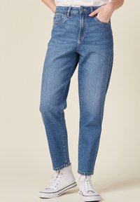Hoge taille blauwe spijkerbroek van denim, met een rechte pijp, opgerolde mouwen en zakken aan de voorkant, gecombineerd met witte hoge sneakers.