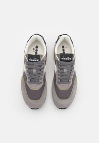 Scarpe da ginnastica grigie e beige che presentano un mix di camoscio e tessuto, lacci rotondi, dettagli a contrasto e un logo sulla linguetta.
