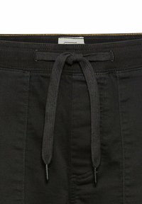 Schwarze Shorts mit einem breiten elastischen Bund und Kordelzug, detaillierter Naht und einer seitlichen Tasche mit glattem Textur.