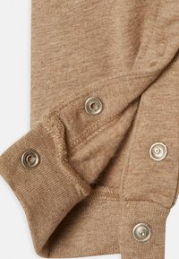 Beige strikstof med metalknapper delvist åbne, der viser den bløde, fuzzy indvendige foring og detaljeret syning på ærmerne.