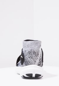 Zadní pohled na šedou a černou pletenou tenisku s bílou podrážkou a černým gumovým vzorkem na bílé ploše.