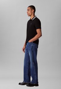 Black polo shirt with white striped collar; paired with blue straight-leg jeans and black shoes, exhibiting a casual fit and clean lines.