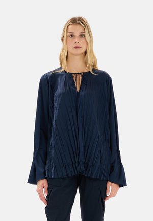 Blusa a maniche lunghe di colore blu navy, realizzata in tessuto morbido, con pieghe verticali, scollo con fiocco e polsini svasati.