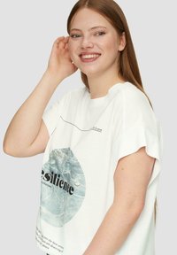 Weißes Baumwoll-T-Shirt mit kurzen Ärmeln, rundem Halsausschnitt und einem grafischen Design in blauer und schwarzer Schrift mit einem kreisförmigen Wasser-Muster.