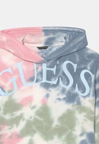 Tie-dye hoodie i rosa, gröna och blå nyanser. Har en stor ljusblå "GUESS"-logga. Tillverkad av mjukt tyg med en ledig passform och hood.