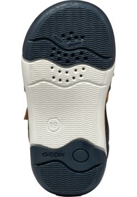 Suela de zapato con una parte superior de goma negra texturizada, media suela blanca y orificios de ventilación. Presenta el logo de Geox y la marca de talla 19.
