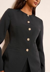 Czarna, dopasowana marynarka z okrągłym dekoltem, sześcioma złotymi, kwiatowymi guzikami i dwoma bocznymi kieszeniami. Gładka faktura tkaniny.