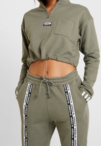 Olivgrön kort sweatshirt med halv dragkedja och bröstficka. Matchad med byxor i jogger-stil med sidostråk och dragsko i midjan.