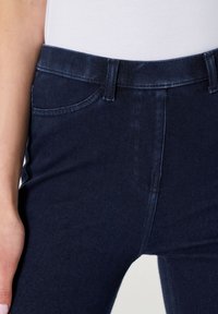 Jeans en denim bleu foncé avec une texture lisse, dotés d'une taille standard, d'un design à cinq poches et de détails de couture minimalistes.