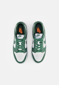 Zapatillas Nike con una parte superior de cuero verde, punta blanca perforada y cordones verdes. La plantilla tiene un logotipo naranja sobre un fondo negro.