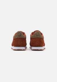 Suede sneakers in burnt orange with a textured olive green heel. White midsole and brown speckled outsole. Simple, athletic design.