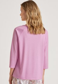 Lichtroze jersey top met driekwart mouwen, ronde halslijn en een ontspannen pasvorm. Zachte textuur, minimalistisch ontwerp, geen zichtbare patronen of accenten.